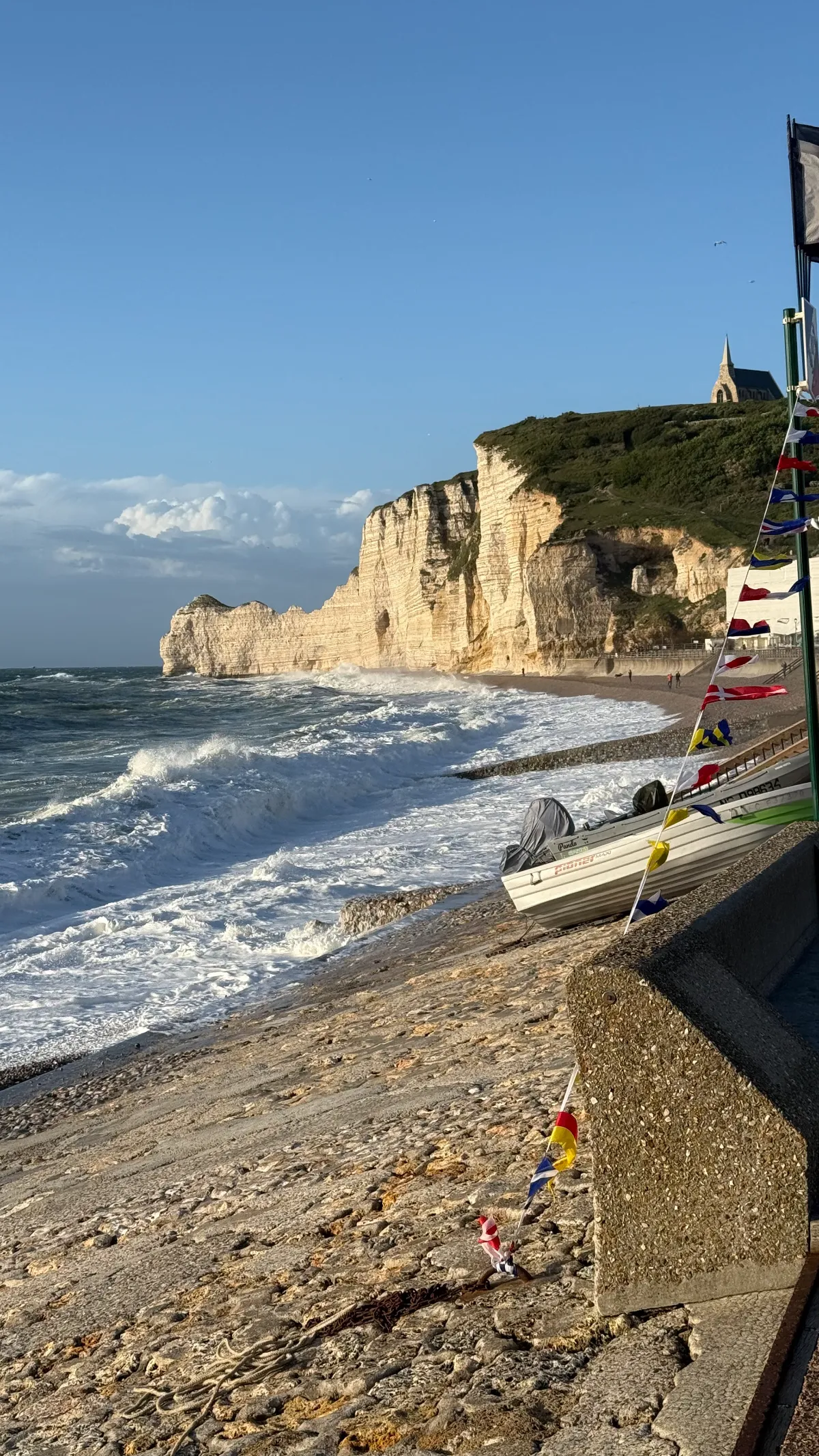 Waves, fishing boats and the sunlit cliffs along the Étretat seafront